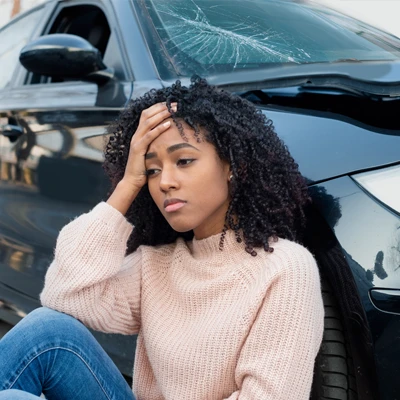 A woman holding her head and leaning against her vehicle after an auto accident